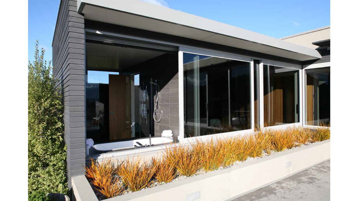 In several of his residential projects Marc Scaife has used a single sliding window system over adjoining rooms. In this wing at Release Retreat the en-suite bathroom (at left in the exterior photo) was spanned by a single panel which withdraws back over a fixed light in the main bedroom. The moving panel on the right of the bedroom also shares the same fixed light.