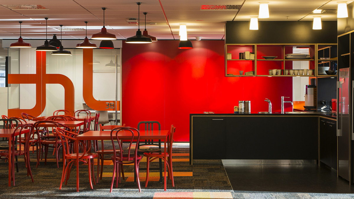 A striking black cruciform-shaped kitchenette is surrounded with a variety of colourful furniture types and styles to create a bright and lively, inviting working hub.