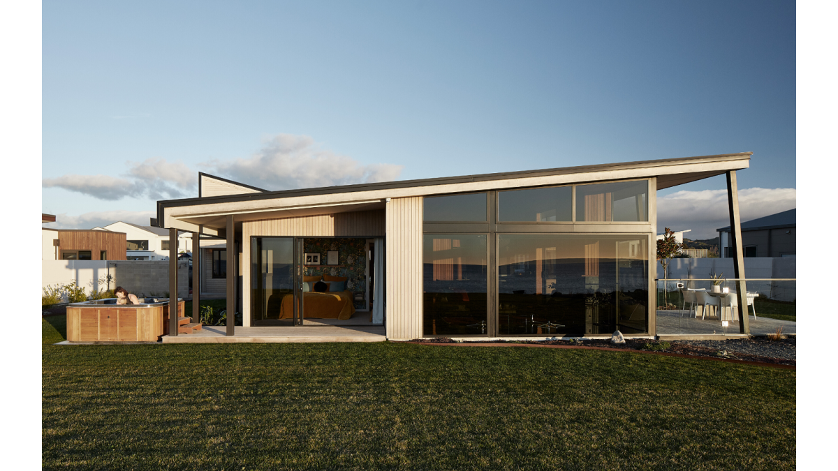 Big picture windows with raked windows above take in the view from the lounge floor to ceiling. The home features redwood timber stained with Dryden WoodOil and is complemented by Matt Black powdercoated aluminium joinery.